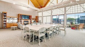 Une pièce spacieuse avec une grande table, des chaises, des étagères et une cheminée.