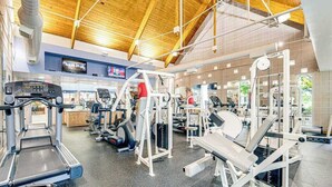 Une salle de sport équipée de tapis de course, d’appareils de musculation et d’un écran de télévision.