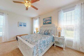 A bedroom with a bed, bedside tables, a ceiling fan, and a window with curtains. - Millville by the sea home w/ shared pool, WiFi, central AC, W/D, & gas fireplace (Millville)