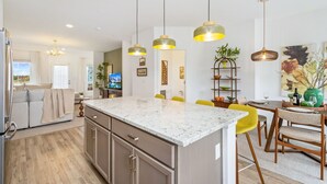 Une cuisine moderne dotée d’un îlot central, de luminaires suspendus et d’un coin repas avec des chaises jaunes.