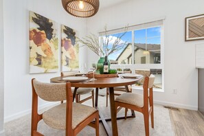 A dining area with a round table, four chairs, and a vase with branches. There are two abstract paintings on the wall.