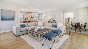 A spacious living room with a sectional sofa, a coffee table, and a dining area with a table and chairs. - Luxe New Home in Tidal Walk - 2 Decks, Home Office, Dogs OK, AC & Shared Pool (Ocean View)