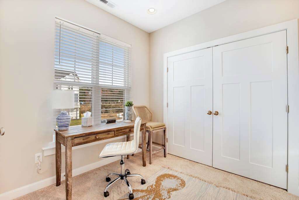 A room with a desk, chair, window with blinds, and a white door.