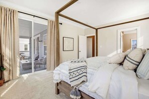 Un dormitori amb un llit amb cortines, una porta corredissa de vidre a un balcó i un quadre al mur.