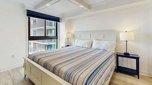 Ein Schlafzimmer mit Bett, Nachttischen, einem Fenster mit Blick und einer Decke mit Einbauleuchten.