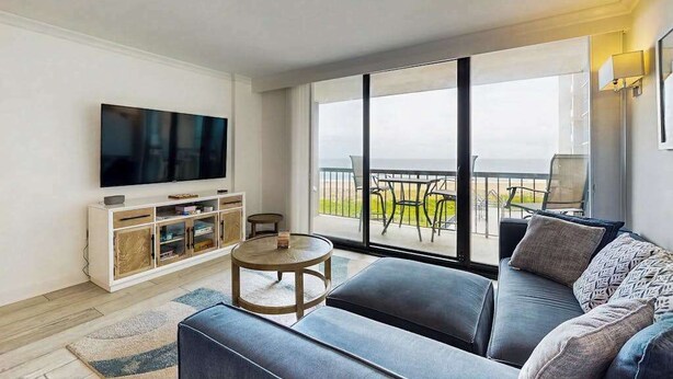 Ein modernes Wohnzimmer mit Flachbildfernseher, einer Couch, einem Couchtisch und einem Balkon mit Gartenmöbeln.