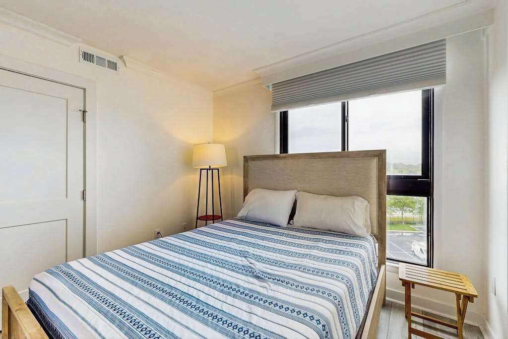 Una camera da letto con un letto, un comodino, una lampada, una finestra e vista sull'esterno.