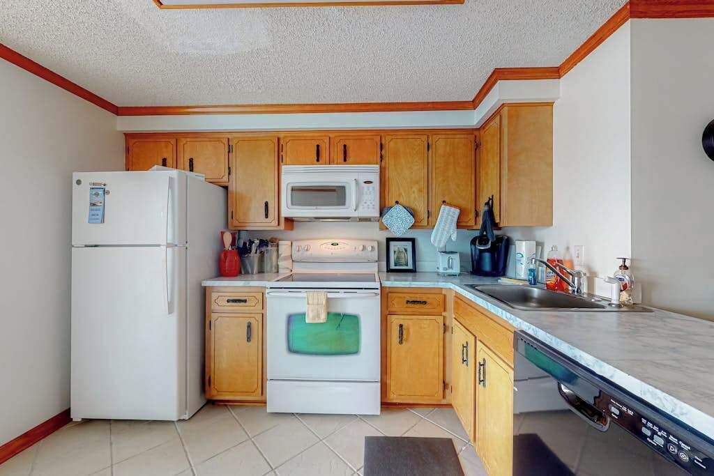 Una cocina compacta con armarios de madera, un refrigerador blanco, un microondas, un horno y un lavavajillas.