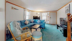 A living room with a sectional sofa, a television, a coffee table, and a wicker chair. - Town of Fenwick Island condo with dazzling sunrise views (Fenwick Island)