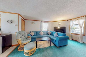 A living room with a blue sofa, a wicker chair, a small table, and a television.