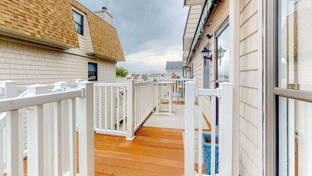 A narrow wooden deck with white railings, a brick building on the left, and a white building on the right. - Town of Fenwick Island condo with dazzling sunrise views (Fenwick Island)