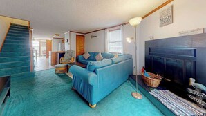 A living room with a blue sofa, a fireplace, a television, and a staircase. - Town of Fenwick Island condo with dazzling sunrise views (Fenwick Island)