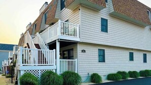 A multi-story building with a brick facade, white siding, and a balcony with a white railing. - Town of Fenwick Island condo with dazzling sunrise views (Fenwick Island)