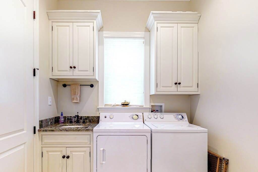 A laundry room with a washer and dryer, white cabinets, a window, and a countertop with a soap dispenser.