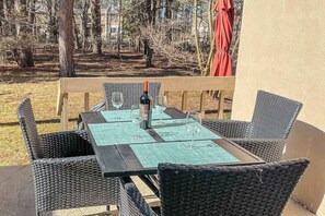 Ein Esstisch mit Stühlen, einer Flasche und Gläsern auf einer Terrasse mit Blick auf Bäume.