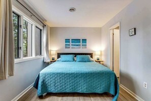 Ein Schlafzimmer mit einem Bett, zwei Nachttischlampen, einem Fenster mit Vorhängen und drei Wandbildern.