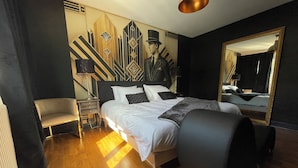 A hotel room with a large bed, a chair, a nightstand, a lamp, and a wall with a geometric pattern. - Le Repaire du Gentleman - Spa, Private Cinema & King-Size Bed • Enclosed Garage (Étretat)