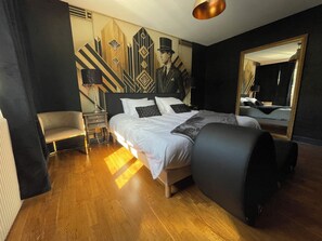 Ein Hotelzimmer mit einem großen Bett, einem Sessel, einem Nachttisch, einer Lampe und einer Wand mit geometrischem Muster.