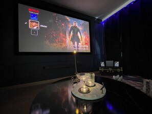A modern living room with a large flat-screen TV mounted on the wall, a decorative glass table with a candle in the center, and a dark-colored sofa. - Romantic Art Deco Suite • Whirlpool Bath • Private Garage • Near the Sea (Étretat)