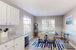 Une cuisine avec des meubles blancs, un plan de travail en granit, une table à manger avec des chaises et un tapis à rayures.