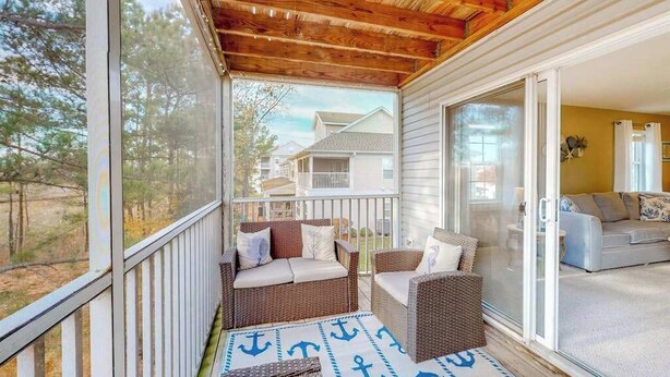 A covered porch with wicker furniture, a view of the neighborhood, and a sliding glass door leading to a living area. - 2nd-floor condo at Bethany Bay with pool, on-site golf, and sports courts (Ocean View)