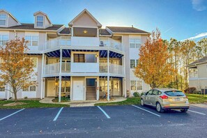 A multi-story residential building with a balcony, a parking lot, and autumn trees. - 2nd-floor condo at Bethany Bay with pool, on-site golf, and sports courts (Ocean View)