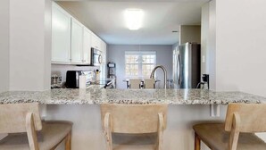 A kitchen with white cabinets, a granite countertop, and a stainless steel refrigerator. - 2nd-floor condo at Bethany Bay with pool, on-site golf, and sports courts (Ocean View)