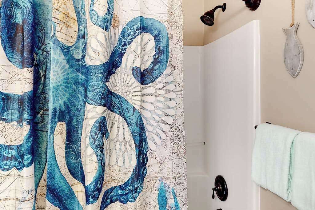 A bathroom with a shower curtain featuring a blue octopus design, a white bathtub, a towel rack with a towel, and a wall-mounted light fixture.