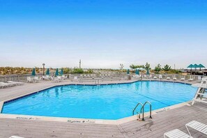 A swimming pool with a deck, lounge chairs, and umbrellas. - Sea Colony Tennis townhouse with pools, tennis, fitness centers, & private beach (Bethany Beach)