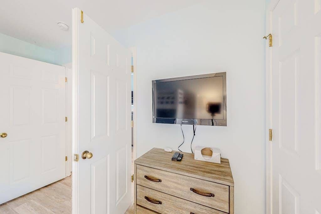A room with a television mounted on the wall, a wooden dresser with drawers, and white doors with brass handles.