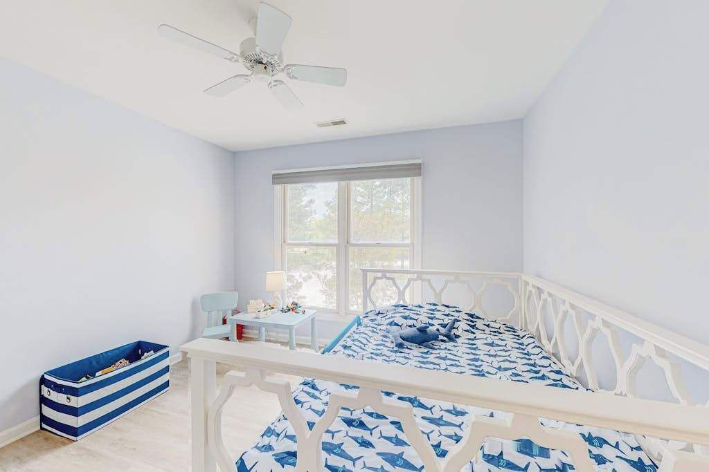 A bedroom with a bed, a nightstand, a desk, a chair, a window, and a ceiling fan.