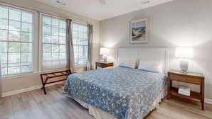 A bedroom with a bed, two bedside tables, a ceiling fan, and a window with curtains. - Bear Trap Dunes home w/ AC, fireplace, balcony, W/D, beach shuttle (Ocean View)