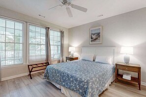 A bedroom with a bed, two bedside tables, a ceiling fan, and a window with curtains. - Bear Trap Dunes home w/ AC, fireplace, balcony, W/D, beach shuttle (Ocean View)