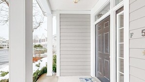 A house entrance with a grey door, a white porch, and a number '5' on the wall. - Bear Trap Dunes home w/ AC, fireplace, balcony, W/D, beach shuttle (Ocean View)