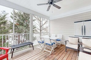 A covered porch with a table and chairs, a ceiling fan, and a view of trees. - Bear Trap Dunes home w/ AC, fireplace, balcony, W/D, beach shuttle (Ocean View)