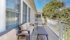 A covered porch with wicker furniture, a view of a house, and a tree. - Bear Trap Dunes home w/ AC, fireplace, balcony, W/D, beach shuttle (Ocean View)
