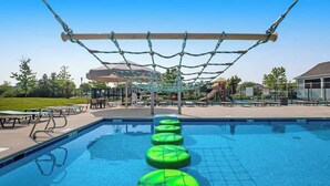 En swimmingpool med en hängbro och gröna, flytande trappsteg.