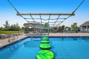 Ein Schwimmbecken mit einer Seilbrücke und grünen, schwimmenden Stufen.