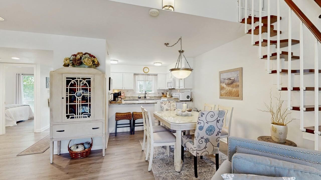 Une cuisine spacieuse avec des meubles blancs, un coin repas doté d’une table et de chaises blanches, et un escalier avec des rampes blanches.