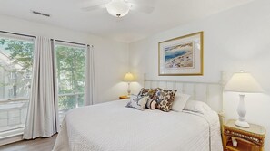 Ein Schlafzimmer mit einem Bett, zwei Nachttischlampen, einem Deckenventilator, einem Fenster mit Vorhängen und einem gerahmten Bild an der Wand.