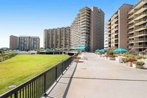 Ein moderner Apartmentkomplex mit mehreren Hochhäusern, einem zentralen Innenhof mit Sitzgelegenheiten und Grünflächen, und blauem Himmel.