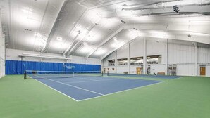 Een indoor tennisbaan met een net, groene vloer en een blauw speelveld.