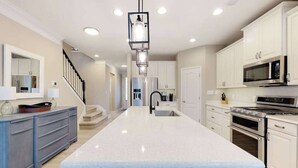 Una cocina moderna con armarios blancos, una isla central, electrodomésticos de acero inoxidable y una lámpara colgante.
