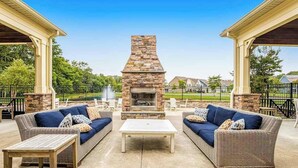 Un patio al aire libre con mobiliario de mimbre, una chimenea de piedra y vistas despejadas del vecindario.