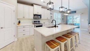 Una cocina moderna con armarios blancos, una isla grande con taburetes e iluminación colgante.