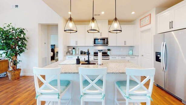 A kitchen with white cabinets, a central island with bar stools, pendant lighting, and a refrigerator. - Bishop's Landing townhouse with grill, outdoor pool, gym, tennis court, shuttle (Millville)