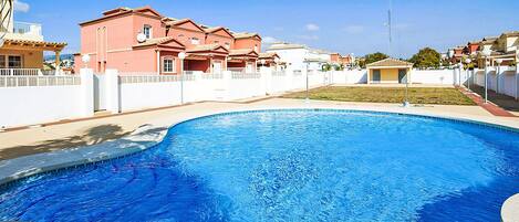 A swimming pool with a clear blue water surface, surrounded by a white fence and a building with a red facade.