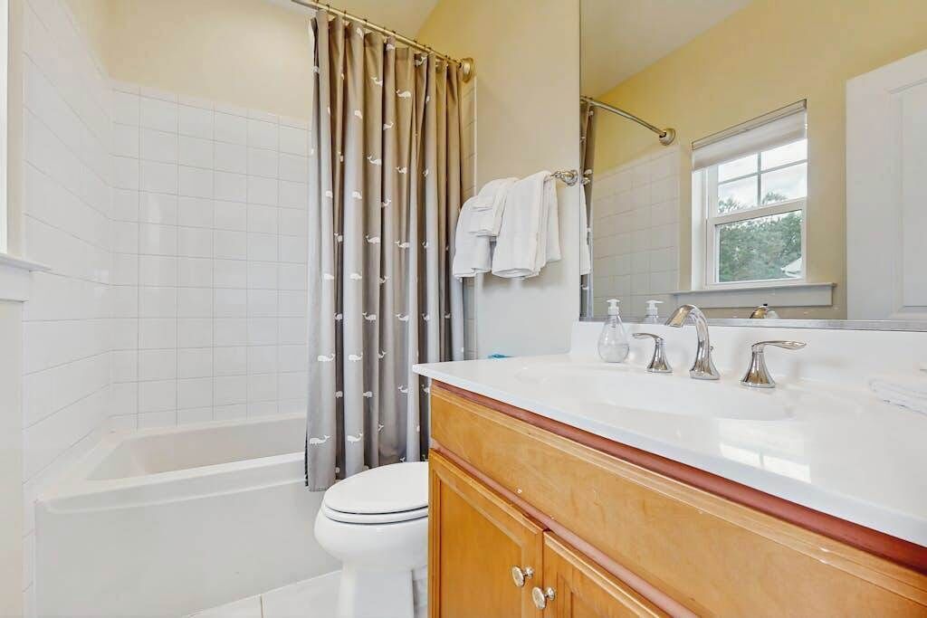 A bathroom with a bathtub, toilet, vanity with a mirror, and a shower curtain.