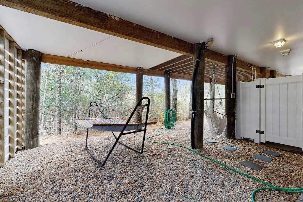 A covered outdoor area with a hammock, a table, and a garden hose.