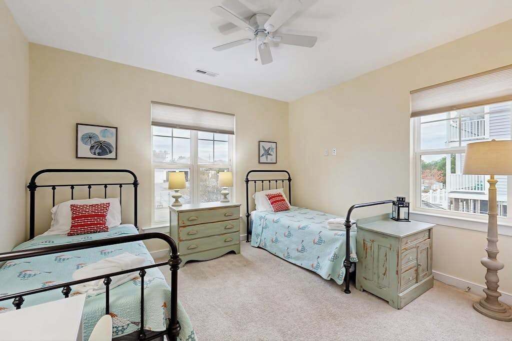 A bedroom with two beds, a dresser, a window, and a ceiling fan.